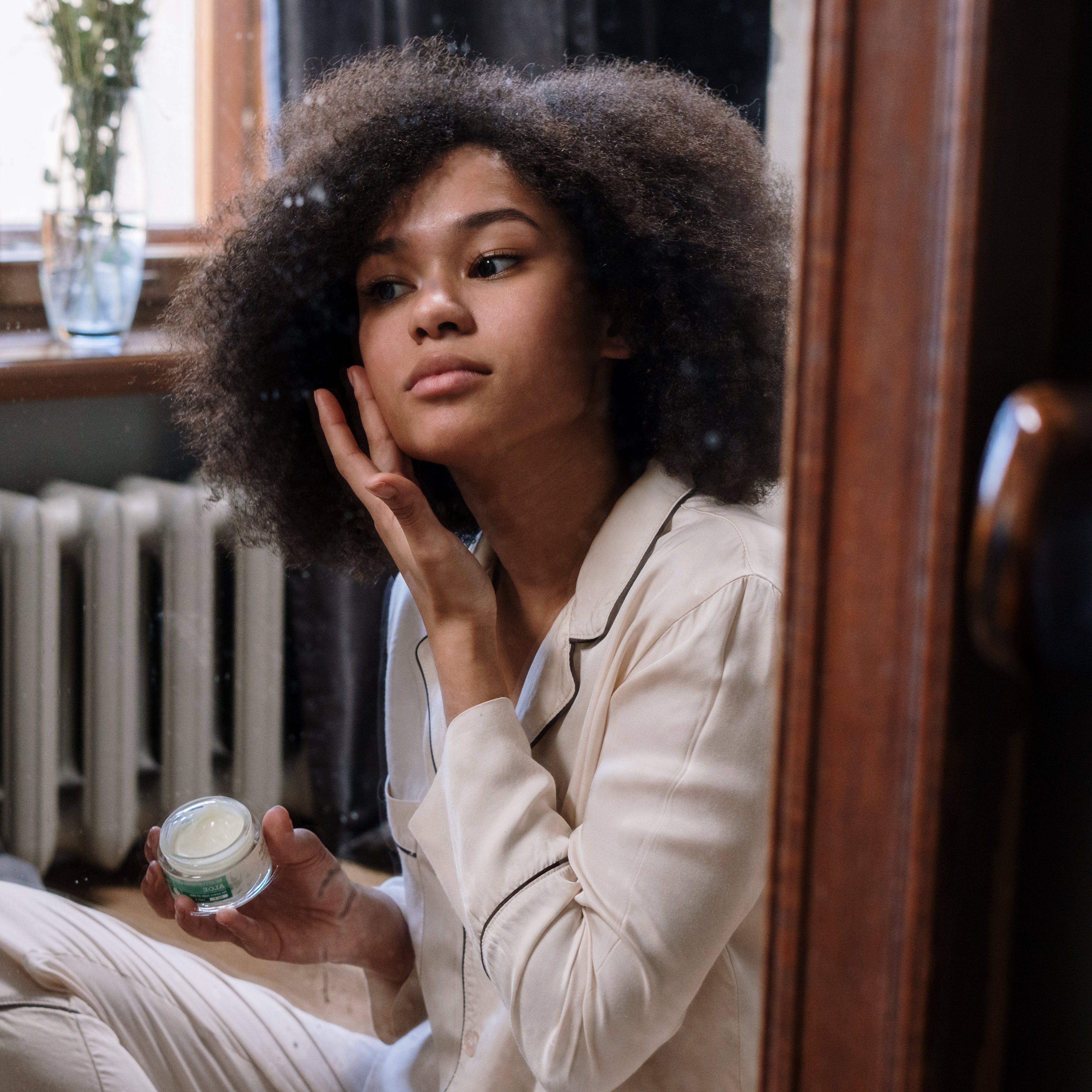 A woman putting on a moisturizer in front of the mirror.